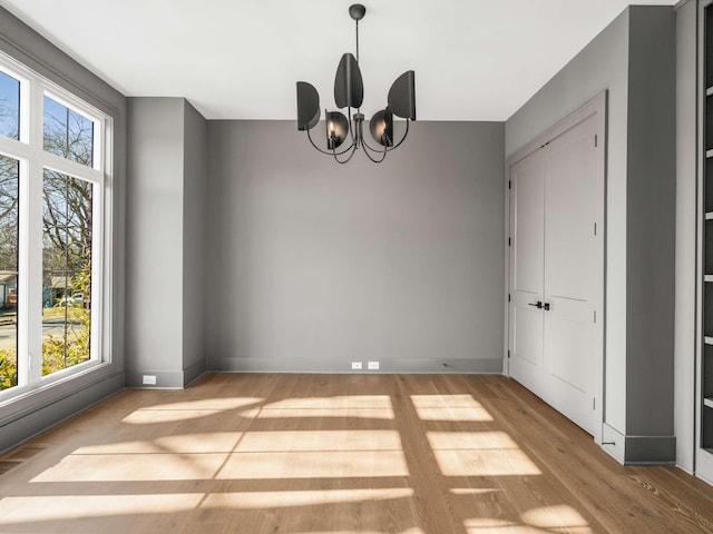 unfurnished dining area featuring a healthy amount of sunlight, an inviting chandelier, and light wood-type flooring