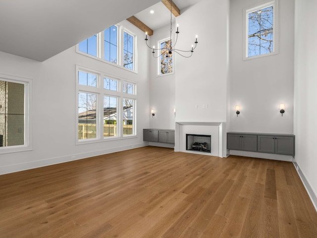 unfurnished living room featuring beamed ceiling, a towering ceiling, hardwood / wood-style floors, and a notable chandelier