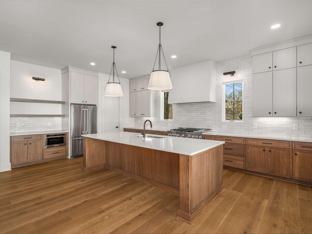 kitchen featuring sink, premium range hood, white cabinetry, stainless steel appliances, and a center island with sink