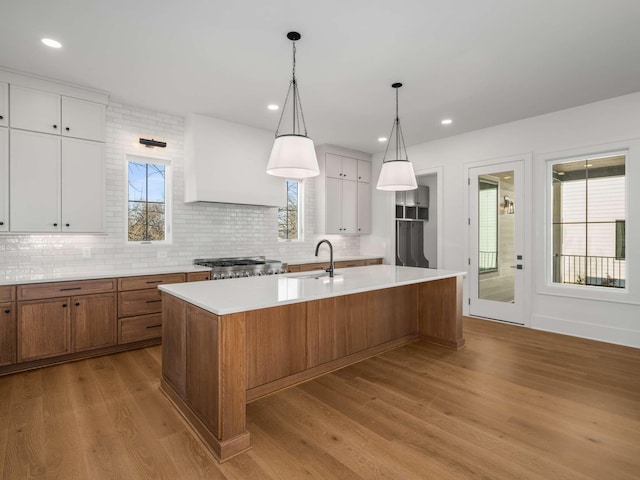 kitchen with premium range hood, sink, a center island with sink, light wood-type flooring, and white cabinets