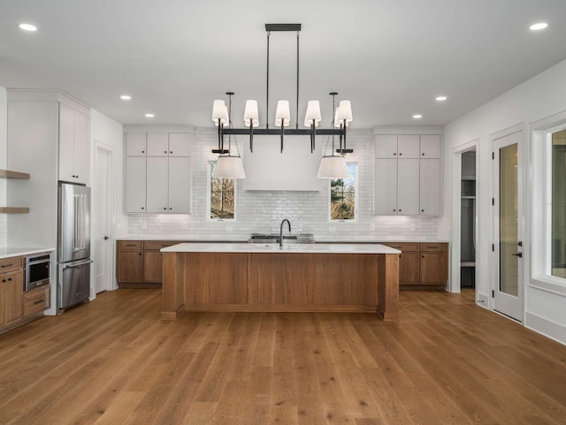 kitchen featuring pendant lighting, light hardwood / wood-style flooring, white cabinetry, high quality fridge, and a center island with sink