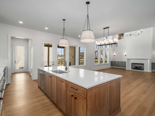 kitchen with pendant lighting, sink, a kitchen island with sink, light hardwood / wood-style floors, and stainless steel dishwasher