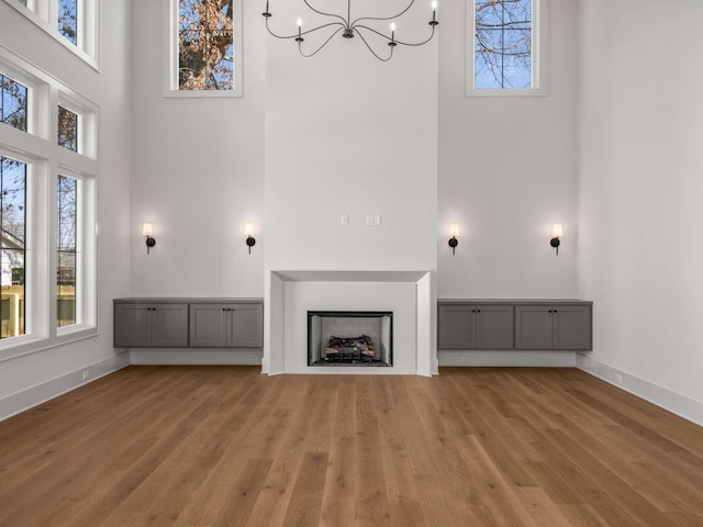 unfurnished living room featuring wood-type flooring, a towering ceiling, and a notable chandelier