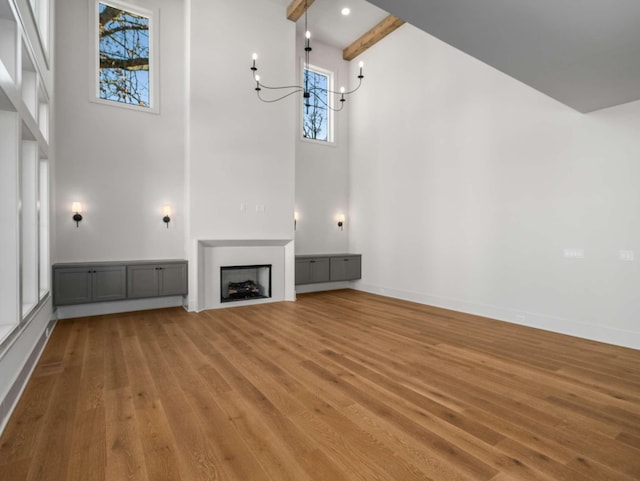 unfurnished living room featuring beam ceiling, a wealth of natural light, light hardwood / wood-style flooring, and a high ceiling