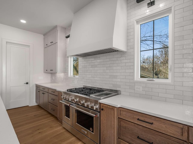 kitchen featuring tasteful backsplash, white cabinetry, custom exhaust hood, double oven range, and light wood-type flooring