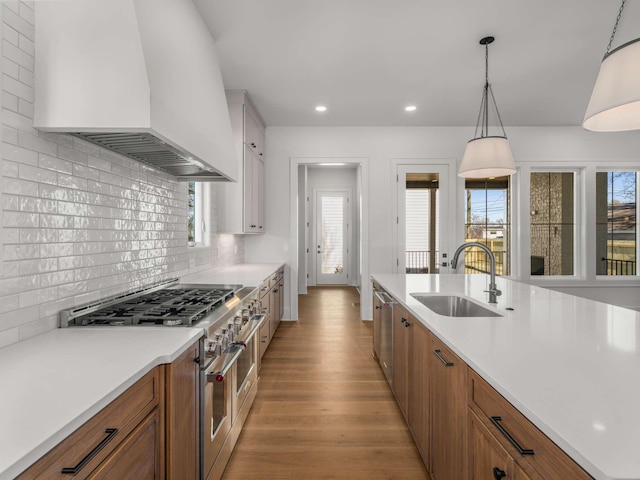 kitchen featuring sink, light hardwood / wood-style flooring, hanging light fixtures, stainless steel appliances, and custom range hood