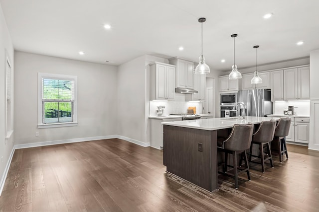 kitchen with appliances with stainless steel finishes, backsplash, white cabinets, a center island with sink, and decorative light fixtures