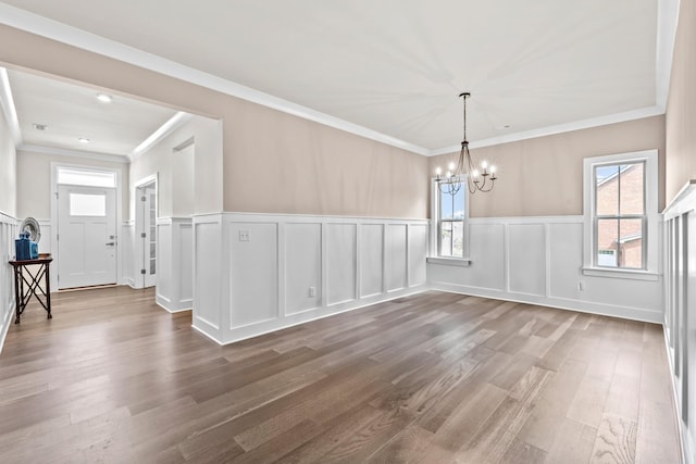 unfurnished dining area with an inviting chandelier, ornamental molding, plenty of natural light, and hardwood / wood-style floors