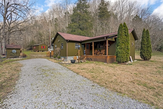 view of front of house featuring covered porch, a front yard, and a storage shed