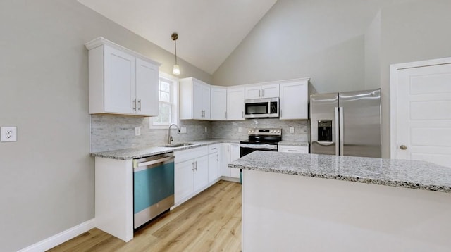 kitchen with high vaulted ceiling, sink, hanging light fixtures, white cabinetry, and stainless steel appliances