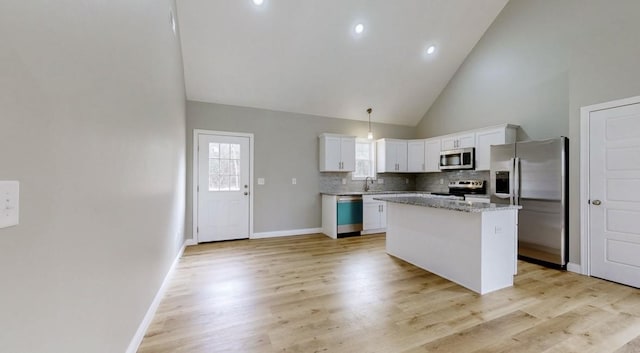 kitchen featuring high vaulted ceiling, white cabinets, appliances with stainless steel finishes, decorative light fixtures, and a kitchen island