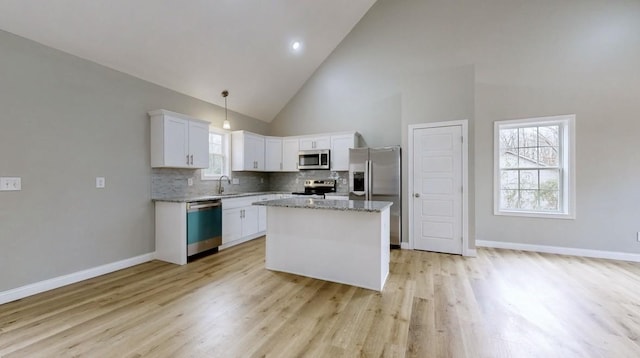 kitchen with appliances with stainless steel finishes, decorative light fixtures, high vaulted ceiling, white cabinets, and a center island