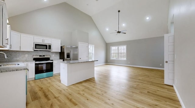 kitchen with appliances with stainless steel finishes, sink, high vaulted ceiling, white cabinets, and a kitchen island