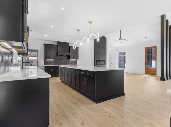 kitchen featuring pendant lighting, light countertops, a kitchen island, wall chimney range hood, and dark cabinetry