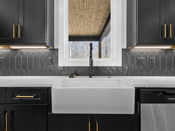 kitchen with dishwasher, backsplash, dark cabinets, light countertops, and a sink