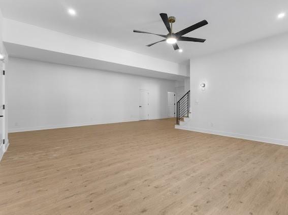 unfurnished living room featuring light wood finished floors, stairs, baseboards, and a ceiling fan