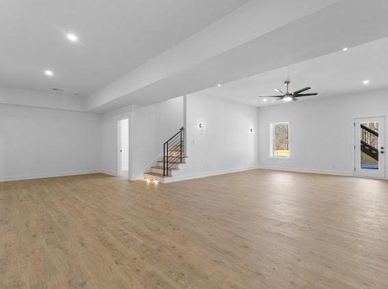 unfurnished living room featuring light wood-type flooring, stairs, baseboards, and a ceiling fan