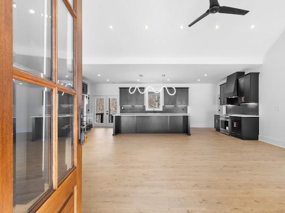 kitchen with dark cabinets, light countertops, wall chimney range hood, and light wood finished floors