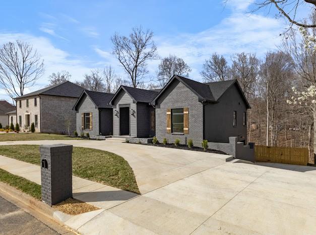 view of front of house with brick siding, curved driveway, a front lawn, and fence