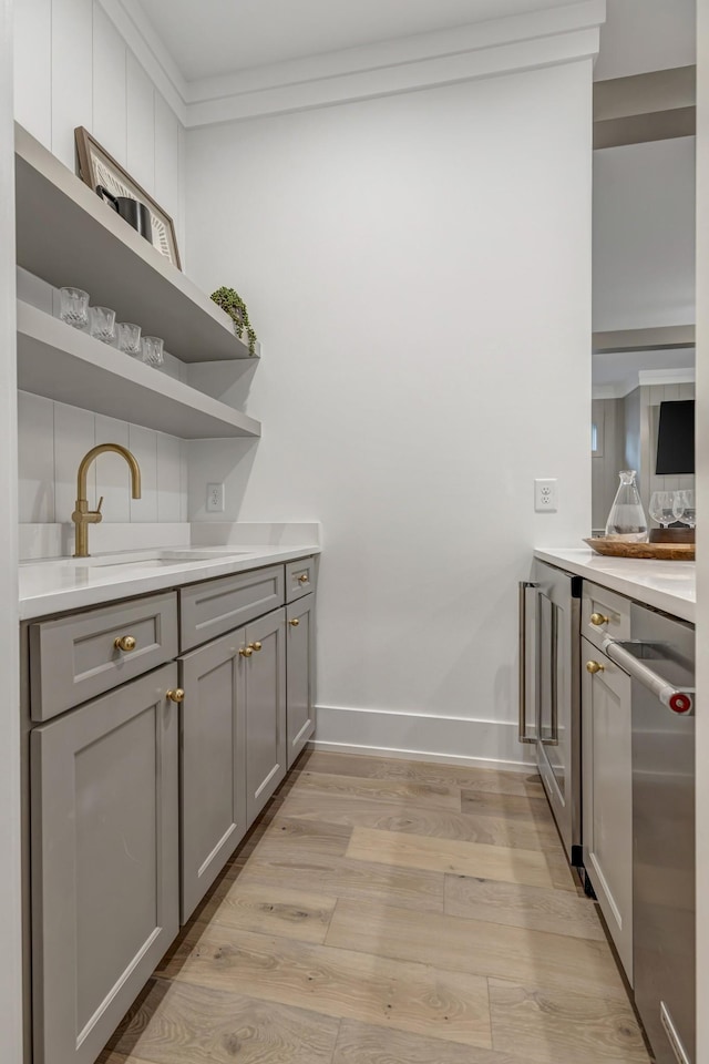 kitchen featuring light hardwood / wood-style floors, gray cabinetry, ornamental molding, stainless steel dishwasher, and sink