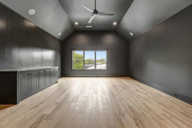 interior space with ceiling fan, vaulted ceiling, wood walls, and light hardwood / wood-style flooring