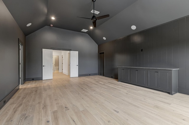 empty room featuring ceiling fan, light wood-type flooring, wood walls, and high vaulted ceiling