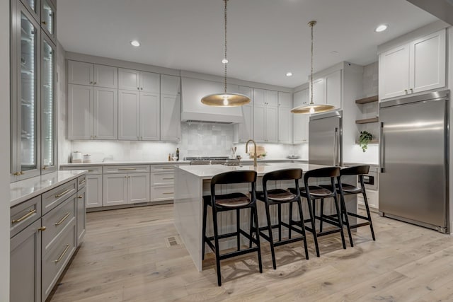 kitchen featuring light hardwood / wood-style floors, pendant lighting, stainless steel appliances, and a center island with sink