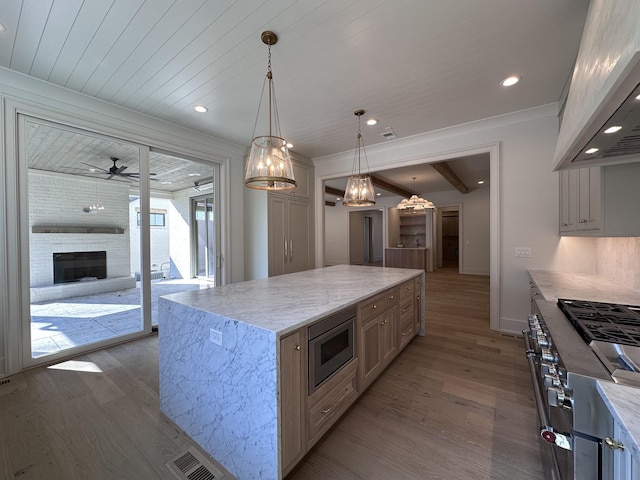 kitchen featuring a brick fireplace, a center island, custom exhaust hood, hanging light fixtures, and appliances with stainless steel finishes