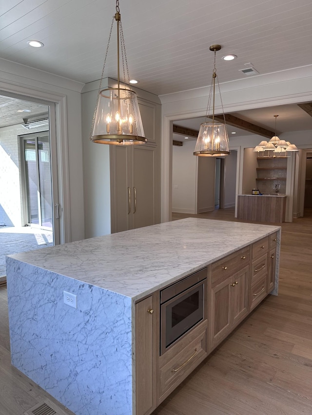 kitchen with stainless steel microwave, decorative light fixtures, a spacious island, and light hardwood / wood-style floors