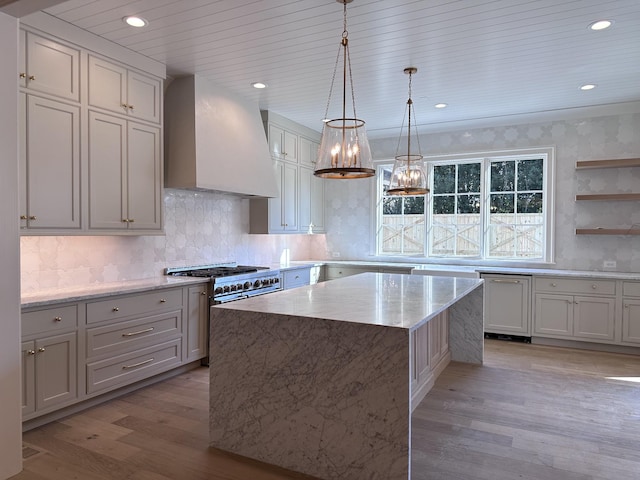 kitchen featuring premium range hood, white cabinetry, light wood-type flooring, hanging light fixtures, and a kitchen island