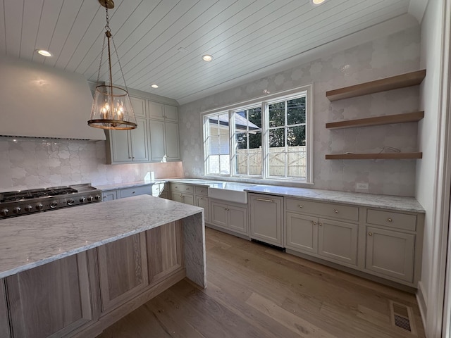 kitchen featuring decorative light fixtures, stove, light stone countertops, light hardwood / wood-style flooring, and wall chimney range hood