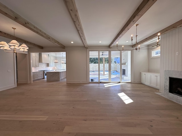 unfurnished living room featuring a fireplace, beamed ceiling, an inviting chandelier, and light hardwood / wood-style flooring