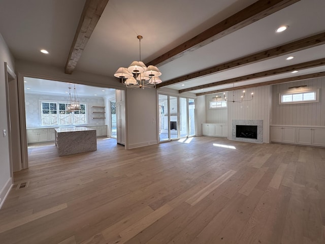 unfurnished living room featuring beam ceiling, a chandelier, and light hardwood / wood-style floors