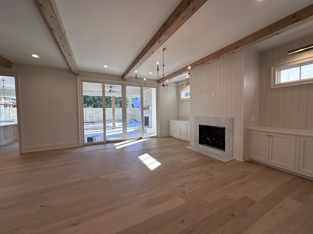 unfurnished living room featuring a high end fireplace, beamed ceiling, an inviting chandelier, and light hardwood / wood-style flooring