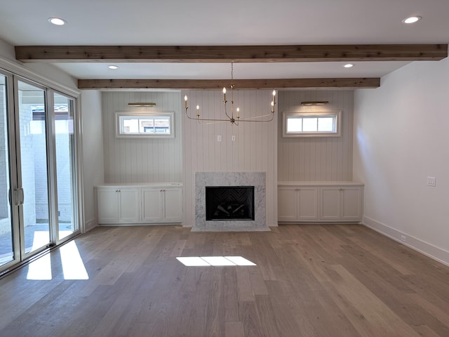 unfurnished living room featuring a healthy amount of sunlight, light wood-type flooring, a notable chandelier, and a premium fireplace