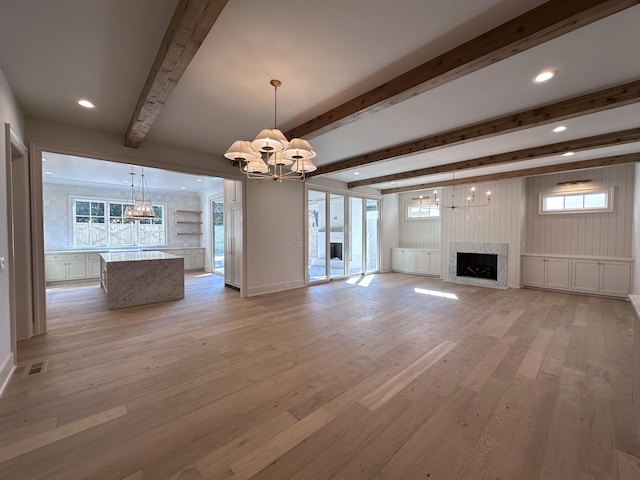 unfurnished living room with beam ceiling, light wood-type flooring, a premium fireplace, and an inviting chandelier