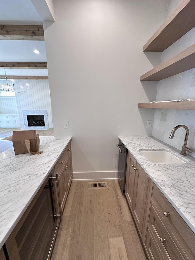 kitchen featuring light hardwood / wood-style floors, stainless steel dishwasher, beam ceiling, light stone counters, and sink