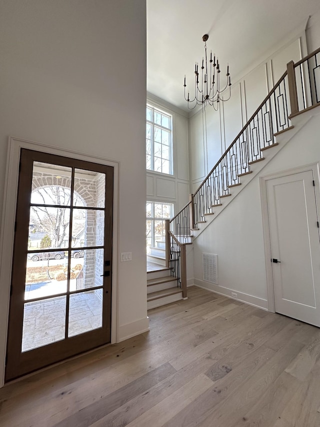 foyer entrance featuring an inviting chandelier, a towering ceiling, and light wood-type flooring