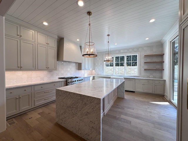 kitchen with double oven range, custom exhaust hood, light hardwood / wood-style floors, hanging light fixtures, and a center island