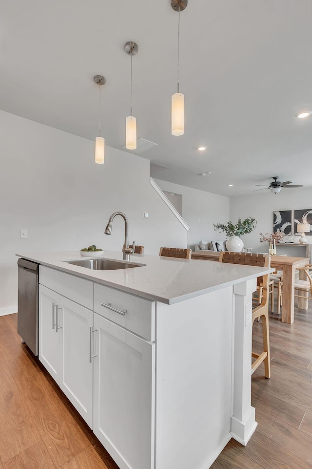 kitchen with sink, hanging light fixtures, stainless steel dishwasher, white cabinetry, and a breakfast bar area