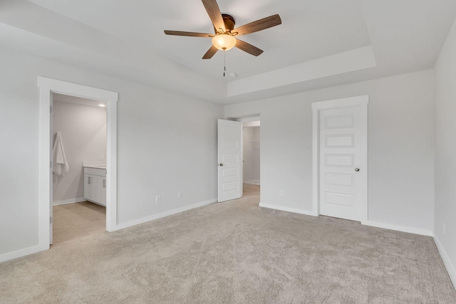 unfurnished bedroom with ensuite bathroom, a raised ceiling, ceiling fan, light colored carpet, and a closet