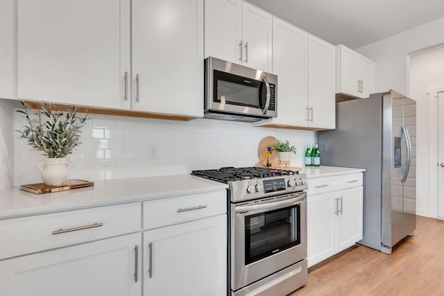 kitchen featuring light hardwood / wood-style flooring, tasteful backsplash, light stone counters, white cabinetry, and stainless steel appliances