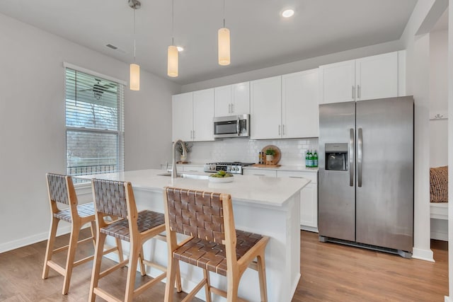 kitchen with tasteful backsplash, an island with sink, pendant lighting, white cabinets, and appliances with stainless steel finishes