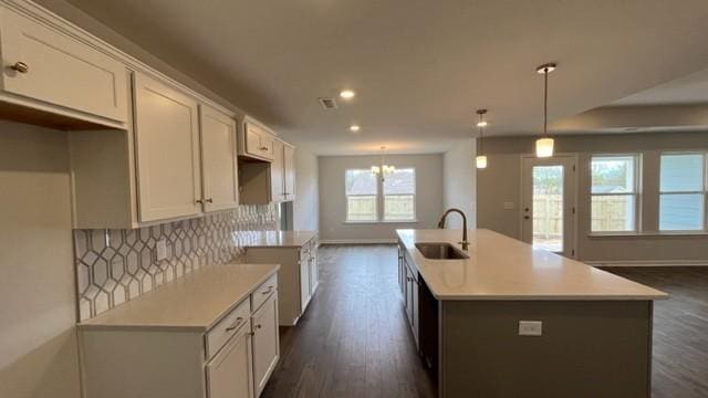 kitchen with tasteful backsplash, sink, decorative light fixtures, white cabinetry, and an island with sink