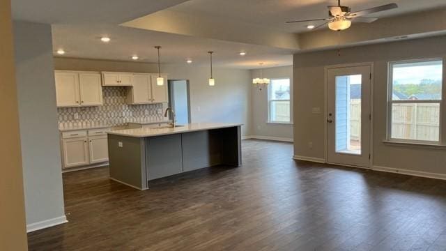 kitchen with pendant lighting, a center island with sink, ceiling fan with notable chandelier, tasteful backsplash, and white cabinetry