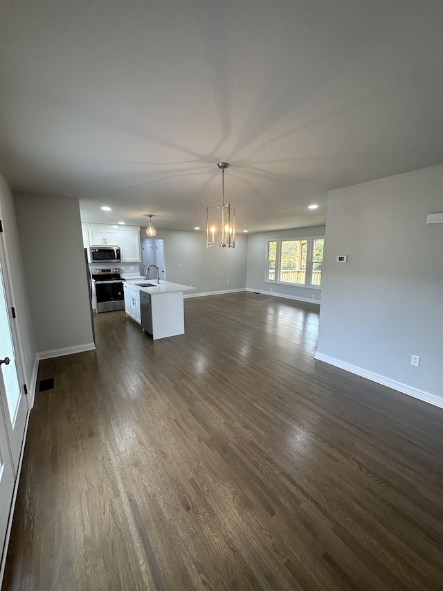 unfurnished living room with an inviting chandelier, dark wood-type flooring, and sink