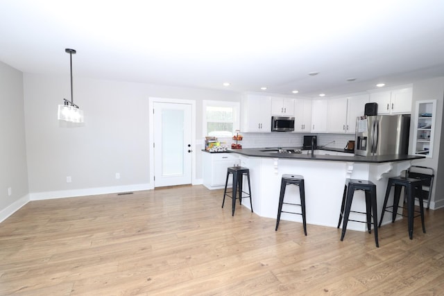 kitchen featuring appliances with stainless steel finishes, a breakfast bar, pendant lighting, white cabinets, and light hardwood / wood-style floors