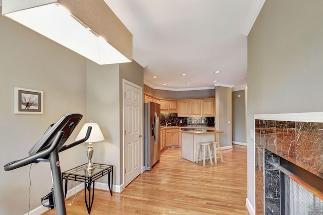 kitchen with a center island, a kitchen breakfast bar, stainless steel refrigerator with ice dispenser, light brown cabinetry, and ornamental molding