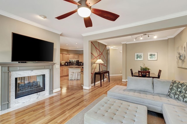 living room with ceiling fan, light wood-type flooring, crown molding, and a high end fireplace