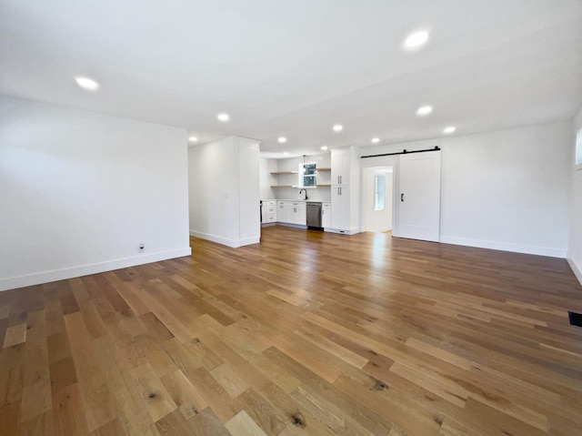 unfurnished living room featuring light wood-type flooring, a barn door, and sink